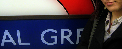 A woman standing by the Bethnal Green sign, seen close-up.